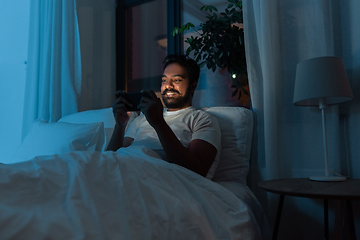 Image showing indian man with smartphone in bed at home at night