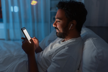 Image showing man with smartphone and earphones in bed at night