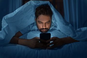 Image showing indian man with smartphone in bed at home at night