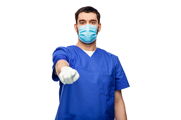 Image showing male doctor in blue scrubs and mask points finger