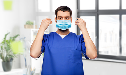 Image showing male doctor in blue uniform putting on mask