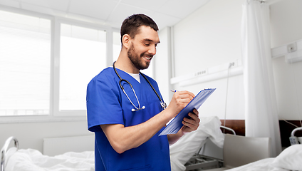 Image showing male doctor writing medical report on clipboard