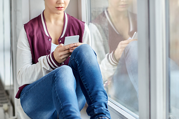 Image showing teenage girl with smartphone sitting on windowsill