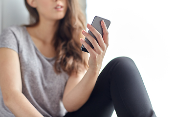 Image showing teenage girl with smartphone sitting at window