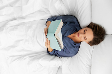 Image showing young woman reading book in bed at home