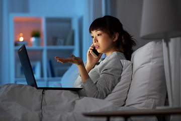 Image showing woman with laptop calling on phone in bed at night