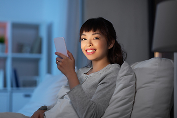 Image showing asian woman with smartphone in bed at night