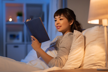 Image showing young asian woman reading book in bed at home