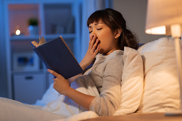 Image showing tired asian woman reading book in bed at home