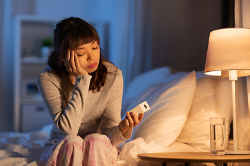 Image showing asian woman with clock sitting on bed at night