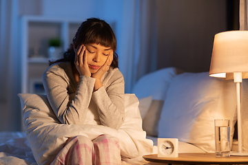 Image showing stressed asian woman sitting on bed at night