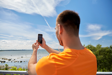 Image showing young man with smartphone and earphones outdoors