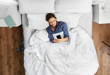 Image showing young woman with smartphone lying in bed