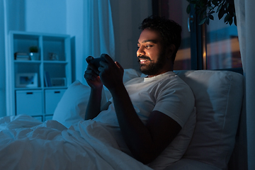 Image showing indian man with smartphone in bed at home at night