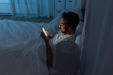 Image showing man with smartphone and earphones in bed at night