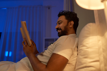 Image showing happy indian man reading book in bed at night