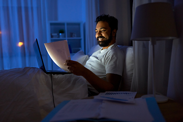 Image showing indian man with laptop and papers in bed at night