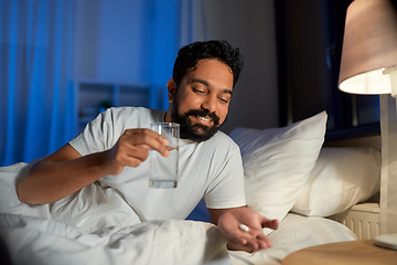 Image showing indian man with medicine and water in bed at night