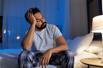 Image showing stressed indian man sitting on bed at night