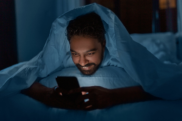 Image showing indian man with smartphone in bed at home at night