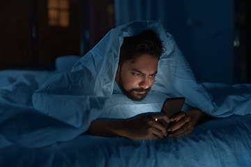 Image showing indian man with smartphone in bed at home at night