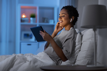 Image showing woman with tablet pc in earphones in bed at night