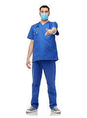 Image showing male doctor in blue scrubs and mask points finger