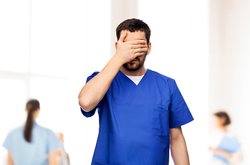Image showing tired doctor or male nurse covering eyes with hand