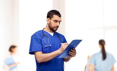 Image showing male doctor writing medical report on clipboard