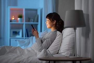 Image showing asian woman with smartphone in bed at night