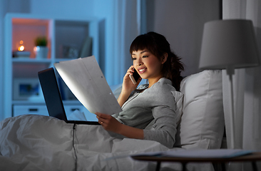 Image showing woman with laptop calling on phone in bed at night