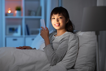 Image showing asian woman with smartphone in bed at night