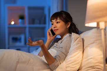 Image showing asian woman calling on smartphone in bed at night