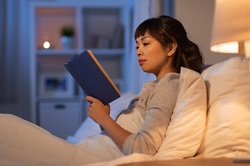 Image showing young asian woman reading book in bed at home