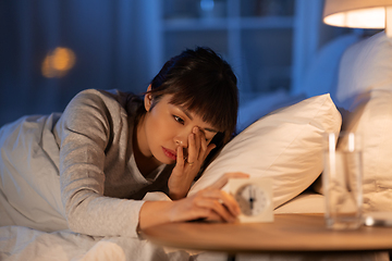 Image showing asian woman with clock lying in bed at night