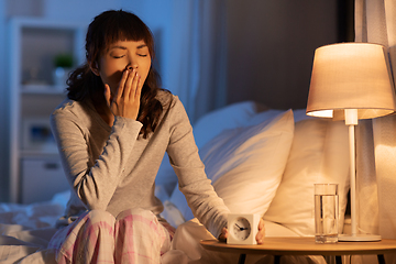 Image showing asian woman with clock yawning in bed at night