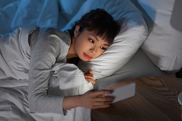 Image showing asian woman with smartphone in bed at night