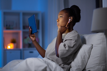 Image showing woman with tablet pc and earphones in bed at night