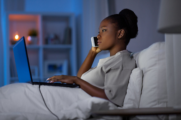 Image showing woman with laptop calling on smartphone in bed