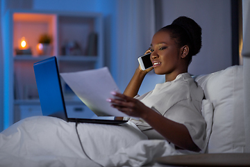 Image showing woman with laptop calling on smartphone in bed