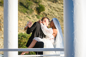 Image showing Young beautiful interracial newlyweds kissing in the gazebo