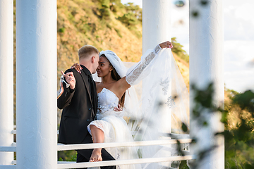 Image showing Young beautiful interracial newlyweds hugging in the gazebo