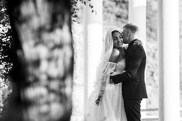 Image showing Portrait of interracial newlyweds hugging against the background of columns, black and white photography