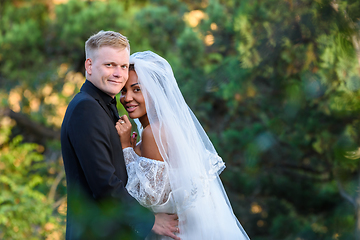 Image showing Portrait of young beautiful interracial newlyweds on green foliage background
