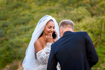 Image showing A black bride accepts congratulations on the phone and looks happily at her white husband