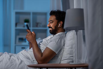 Image showing man with smartphone and earphones in bed at night