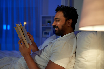 Image showing happy indian man reading book in bed at night