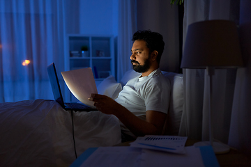 Image showing indian man with laptop and papers in bed at night