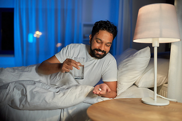 Image showing indian man with medicine and water in bed at night