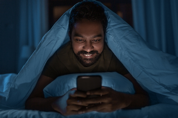 Image showing indian man with smartphone in bed at home at night